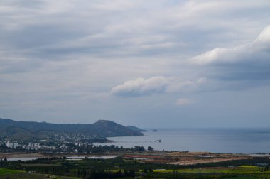 Sergilenen sakin manzaralar yemyeşil yemyeşil bulutlu bir gökyüzünün altında sakin denizle buluşuyor, bir anlık bir yansımayı davet ediyor..