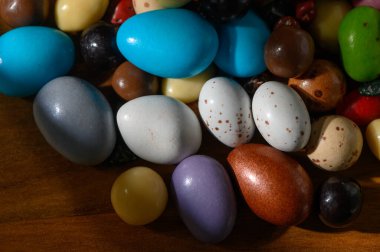 Canlı renklere sahip çeşitli dekoratif yumurtalar sıcak ahşap bir yüzeye dağılmış ve neşeli bir ortam yaratıyor..