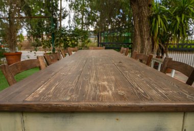 Kırsal bir ahşap masa, ağaçların altında toplanan güzel bir öğleden sonra için arkadaşları ve ailesini bekliyor..