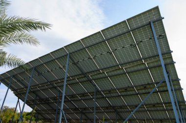 Güneş panelleri gökyüzüne karşı dik duruyor, verimli, yeşil bir ortamda sürdürülebilir enerji çözümleri sergiliyorlar..