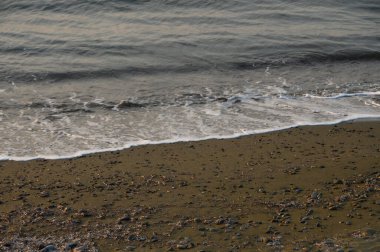 Karanlık çöktüğünde, yumuşak dalgalar taşlı bir sahile yuvarlanır ve suyun kenarında sakin bir atmosfer oluşturur..