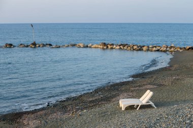 Yalnız bir şezlong kumlu sahilde oturuyor, alacakaranlıkta sakin sulara bakıyor, rahatlamaya ve yalnızlığa davetiye çıkarıyor..