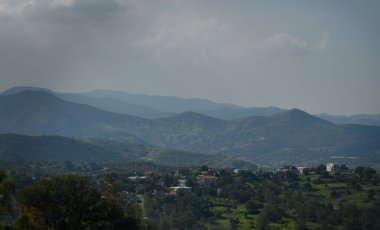 yemyeşil tepeler sakin bir köyü kucaklıyor, bulutlu bir gökyüzünün altında görkemli dağlara karşı kurulmuş, huzuru çağrıştırıyor..