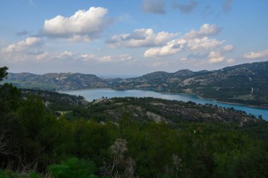 Bereketli bir göl, sakin bir öğleden sonra yukardaki yumuşak bulutları yansıtan yemyeşil bir gölün etrafını sarar..