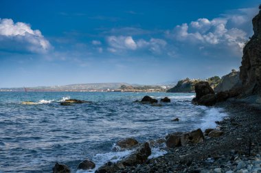 Dalgalar kayalık kıyılara çarpıyor bulutlar gökyüzüne doğru sürükleniyor ve güzelliklerle dolu sakin bir kıyı manzarası yaratıyor..