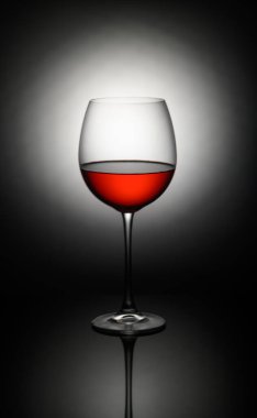 Zengin kırmızı şarap kadehleriyle dolu kristal berrak bir bardak karanlık bir zemin karşısında çarpıcı yansımalar sergiliyor..