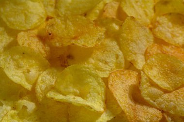 Koyu kahverengi patates cipsleri serpilmiş, çıtır çıtır dokularının ve lezzetli lezzetlerinin tadını çıkarmaları için aperatifleri davet ediyor..