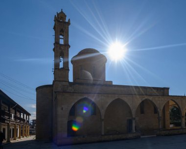 Huzurlu bir köydeki tarihi taş binaların üzerinde gün ışığı parıldıyor. Karmaşık detaylar ve sükunet vurgulanıyor..