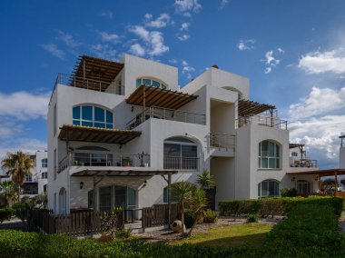 Güzel bir sahil villası, açık mavi gökyüzünün altında canlı yeşilliklerle çevrili modern mimariyi sergiliyor..