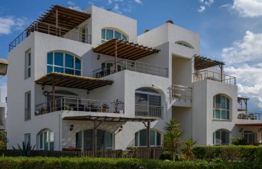 Geniş pencereli ve teraslı çağdaş binalar tropikal bitkiler ve mavi gökyüzünün ortasında güneşlenirler..