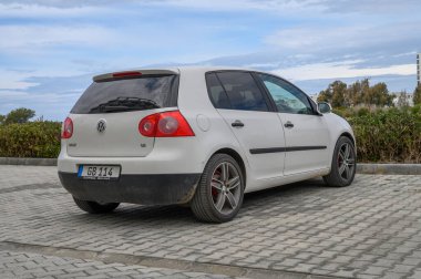 Gaziveren Kıbrıs Rum Kesimi -28.02.2025 Yumuşak dalgalar ve bulutlu gökyüzü sakin bir kıyı atmosferi yaratırken küçük bir araba kaldırım taşının üzerinde duruyor.