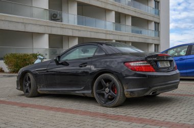 Gaziveren Kıbrıs Rum Kesimi -28.02.2025 Parlak güneşin altında parlak siyah bir üstü açık araba modern bir arkaplan karşısında zarif tasarımını sergiliyor.