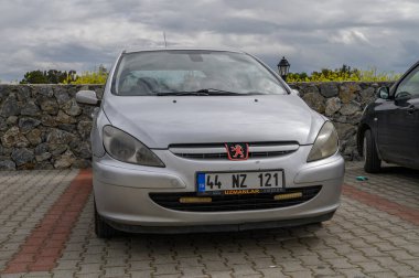 Gaziveren Kıbrıs Rum Kesimi -28.02.2025 Gümüş bir hatchback, yemyeşil ve taş duvarların arasında duruyor.