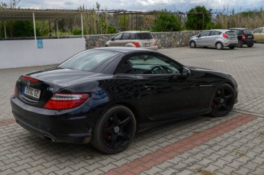 Gaziveren Kıbrıs Rum Kesimi -28.02.2025 Yeşil ve bulutlarla çevrili, üstü açık şık bir siyah araba park halinde duruyor..