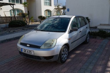 Gaziveren Kıbrıs Rum Kesimi 01.03.2025. Güneş ışığında yeşil çerçeveli bir avluda oturan gümüş bir hatchback, sakin bir sahil geri çekilme havasını çağrıştırıyor..