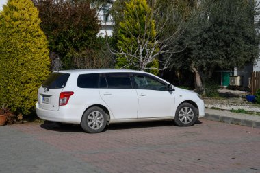 Gaziveren Kıbrıs Rum Kesimi 01.03.2025 Huzurlu, güneşli bir yerleşim bölgesinde canlı bir çalılığın yanında beyaz bir steyşın vagon dinleniyor.