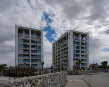 Parlak yapılar, yemyeşil ve bulutlar tarafından kucaklanan kayalık arazi üzerinde yükselir ve modern yaşamın sinyallerini verir..