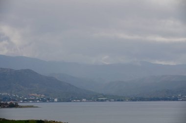 Sakin bir göl yumuşak renkleri yansıtır. Yüksek dağlar arka planda kalır. Sis ve bulutlarla kaplanır..