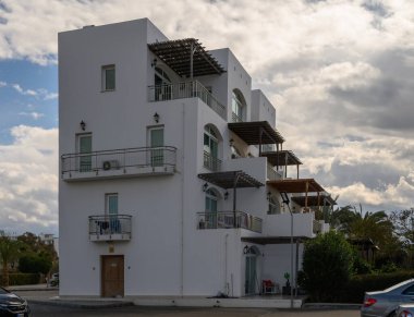 Çağdaş bir beyaz bina balkonları ve yeşillikleri sergiliyor, deniz kenarında sakin bir atmosfer yaratıyor..