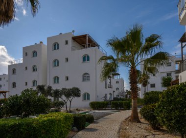 Bereketli yeşillik ve palmiye ağaçlarıyla çevrili beyaz mimari tasarımların yer aldığı büyüleyici tatil köyü manzarası..