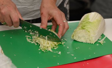 Yetenekli eller canlı yeşil bir tahta üzerinde taze lahana doğradı, mutfak aktivitelerinin canlı atmosferiyle çevrili..