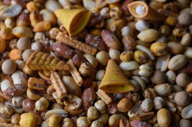 Fındık ve çıtır çıtır yiyeceklerden oluşan canlı bir karışım, ahşap bir yüzeyi dolduruyor, sıcak bir mutfağın sıcak tonlarını vurguluyor..