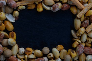 Çeşit çeşit fındık ve atıştırmalık elementlerin hoş bir karışımı karanlık bir merkezin etrafını sarar, davetkar ve zengin bir görsel doku yaratır mutfak sunumları için mükemmel.