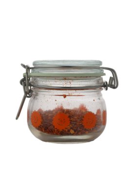 Canlı turuncu çiçeklerle süslenmiş büyüleyici bir cam kavanoz ezilmiş kırmızı biber taneleri içerir, ahşap mutfak tezgahında dinlenir sıcak öğleden sonra ışığında yıkanır, mutfak keşiflerini teşvik eder..