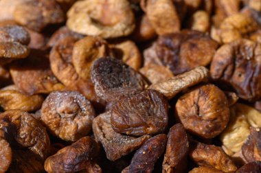 Kurumuş incirlerden oluşan canlı bir görüntü, sıcak güneş ışığı altında parlak yüzeylerini ve zengin renklerini gözler önüne sererek, yoldan geçenleri doğal tatlılıklarını ve dokularını takdir etmeye davet ediyor..