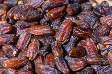 Luscious, koyu kahverengi kurumuş hurma yığınları yüksek, parlak yüzeyleri hareketli bir Orta Doğu pazarının sıcak ışığını yakalıyor, bölgenin zengin kültür ve lezzetlerini çağrıştırıyor.
