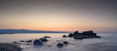 Sahil şeridini saran dingin alacakaranlık yumuşak taşları aydınlatırken yumuşak dalgalar hafifçe onlara çarpar..