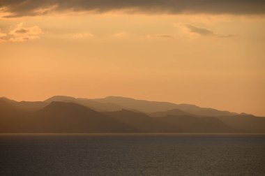 Altın renkler gökyüzünü boyar dalgalar yavaşça kıyı kayalıklarına çarpar gün batımında.