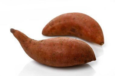 Kırmızımsı kahverengi renkli iki tatlı patates zarif bir şekilde sergileniyor, organik formlarını ön plana çıkarıyorlar..