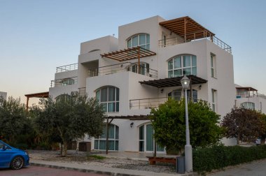 Yuvarlak hatları olan zarif çok katlı bina yeşilliklerle çevrili sakin bir akşam gökyüzüne karşı duruyor..