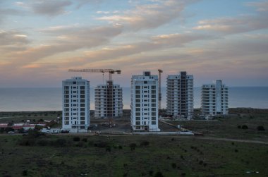 Modern dairelerin inşaatı, kıyı şeridinin üstündeki akşam gökyüzünde sürüklenen bulutlar gibi ılık bir parıltıyla parlıyor..