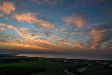 Çarpıcı bir günbatımı sıcak renklerle gökyüzünü aydınlatır. Sakin sulara ve çevreleyen alanlara yansıtır..
