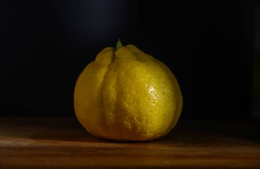 Güzel şekilli sarı bir limon, ahşap bir masanın üzerinde oturuyor. Dokusunu ve rengini vurgulamak için nazikçe aydınlatılmış..