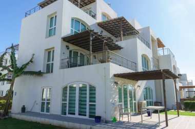 Çağdaş bir villa, berrak mavi gökyüzünün altında balkonlarla ve yemyeşil yeşilliklerle övünür. Rahatlığı ve rahatlığı davet eder..