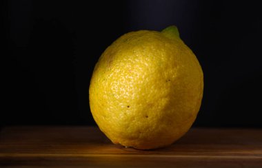Canlı sarı bir limon pürüzsüz bir ahşap yüzeyde, çarpıcı bir karanlık zemine karşı, dikkatleri üzerine çeker..