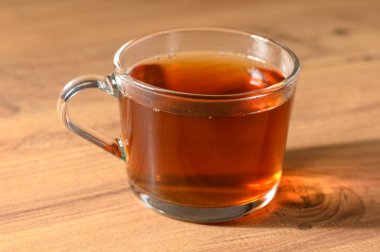 Parlak ahşap bir yüzeye oturmuş aromatik bitki çayıyla dolu berrak bir cam bardak sıcaklığı ve teselliyi davet ediyor..