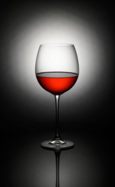 Zengin kırmızı şarap kadehleriyle dolu kristal berrak bir bardak karanlık bir zemin karşısında çarpıcı yansımalar sergiliyor..