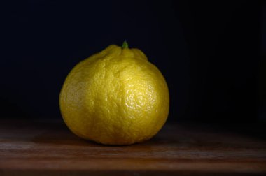 Parlak sarı limon, ahşap bir tahtanın üzerinde huzur içinde oturur. Yumuşak bir ışığın loş ışığında yumuşakça parlayan dokusu.