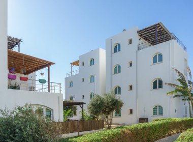 Canlı mimari, açık mavi gökyüzünün altında yemyeşil bitkilerle çevrili parlak beyaz duvarlara sahiptir..