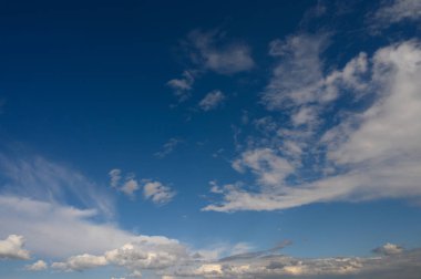 Geniş mavi gökyüzü yumuşak, beyaz bulutlarla kaplı öğleden sonra ışığında sakin bir atmosfer yaratıyor..