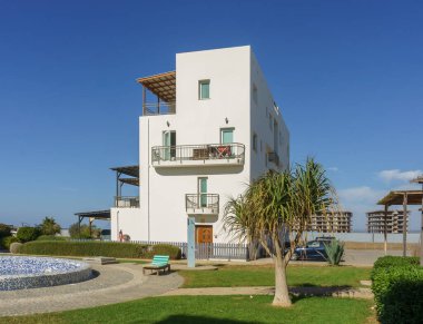 Modern beyaz bir bina canlı bir yeşilliğin ortasında duruyor, mükemmel bir sahil çekilmesinin özünü yakalıyor..