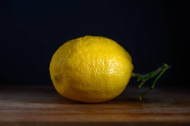 Canlı bir limon, yumuşak ışık altında pürüzsüz ve dokulu derisini sergilerken tahta bir tahtanın üzerinde huzur içinde oturur..