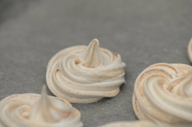 Zarif krema kıvrımları parşömen üzerinde duruyor, sıcak bir mutfakta tatlı, havadar şekerlemelere dönüşmeye hazır..