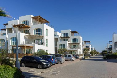 Sersemletici beyaz binalar huzurlu bir caddede berrak bir gökyüzünün altında huzurlu bir kıyı manzarası sunuyor..