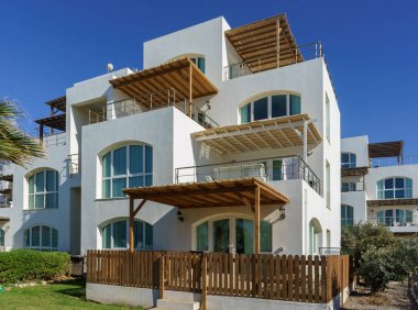 Bu zarif sahil evinde geniş balkonlar, ahşap çitler ve renkli yeşillikler var..