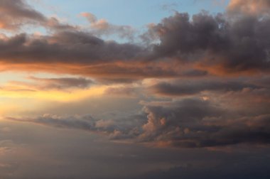 Bulutlar akşam gökyüzünde zarifçe yuvarlanırken, altın renkler derin mavilerle harmanlanır ve nefes kesici bir atmosfer yaratır..